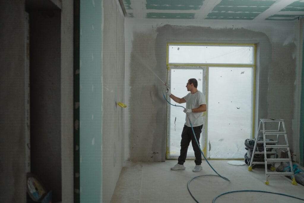 Illustrative library photograph, not an Elbaz project: a worker spraying around a door opening in a stripped commercial room