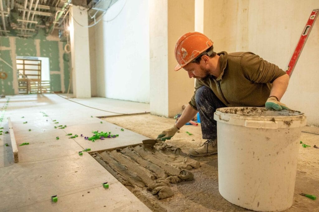 Illustrative library photograph, not an Elbaz project: a tiler bedding floor tile in a commercial space under renovation
