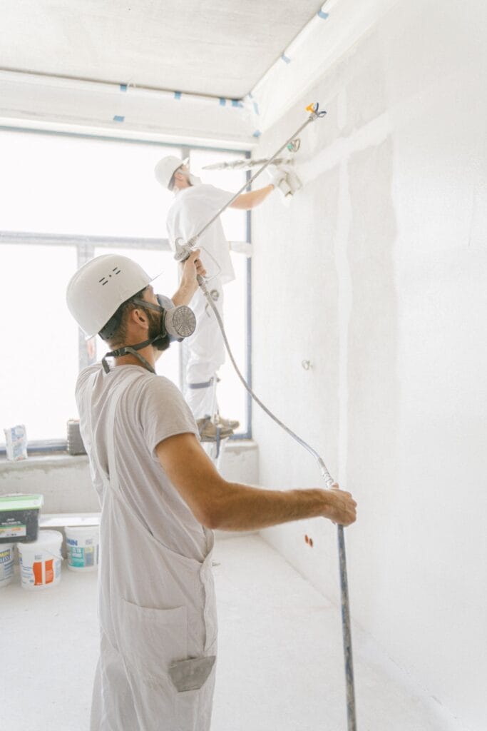 Illustrative library photograph, not an Elbaz project: painters spraying a wall inside a commercial interior during a fit-out