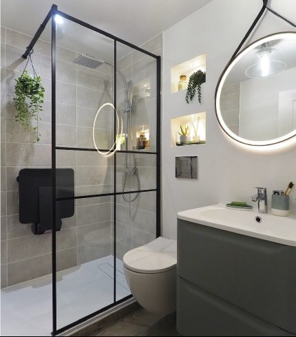 Renovated bathroom with frameless glass shower and round backlit mirror