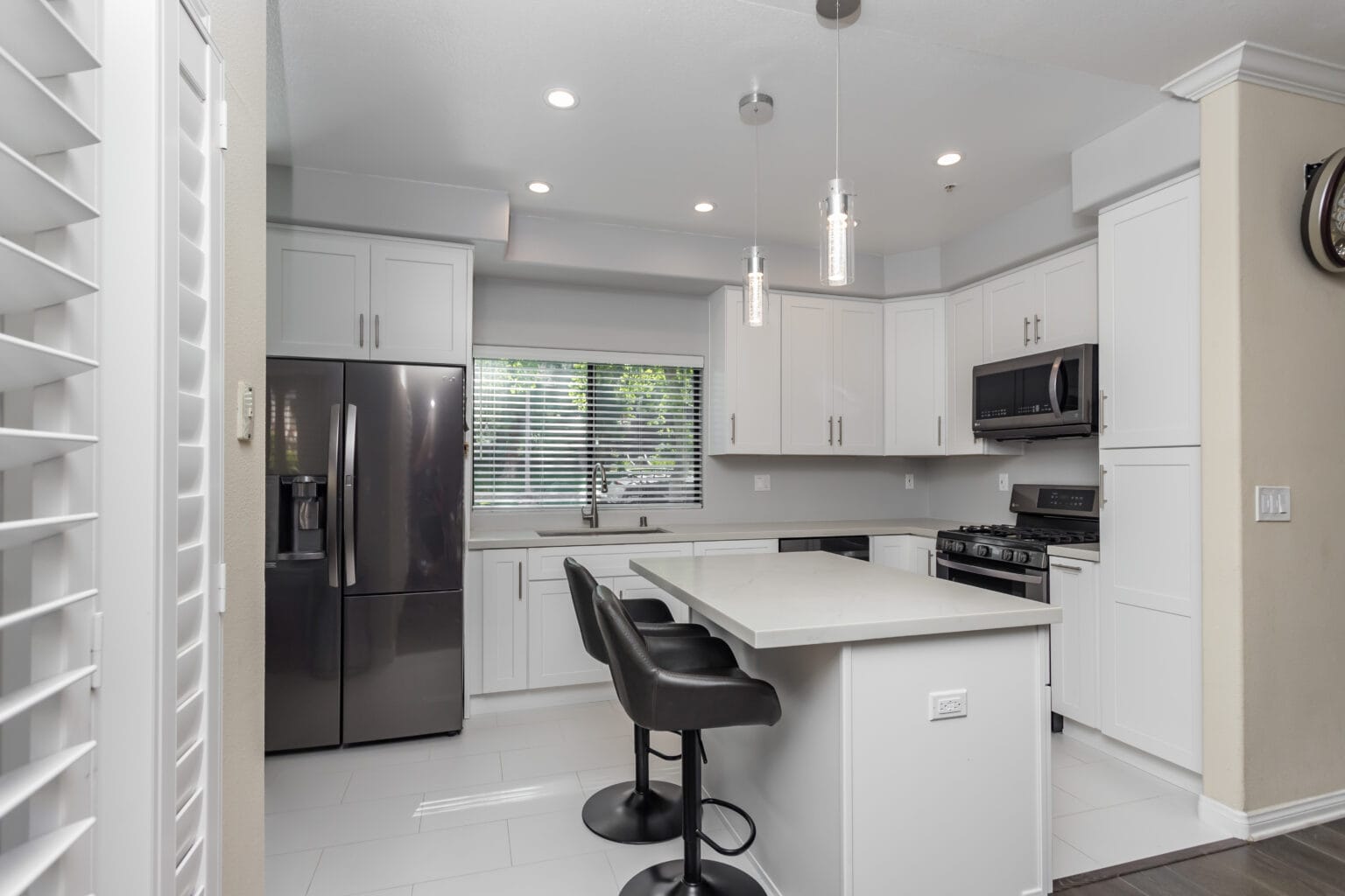 The same kitchen from the living side, with a quartz island, pendant lighting and a stainless fridge-freezer