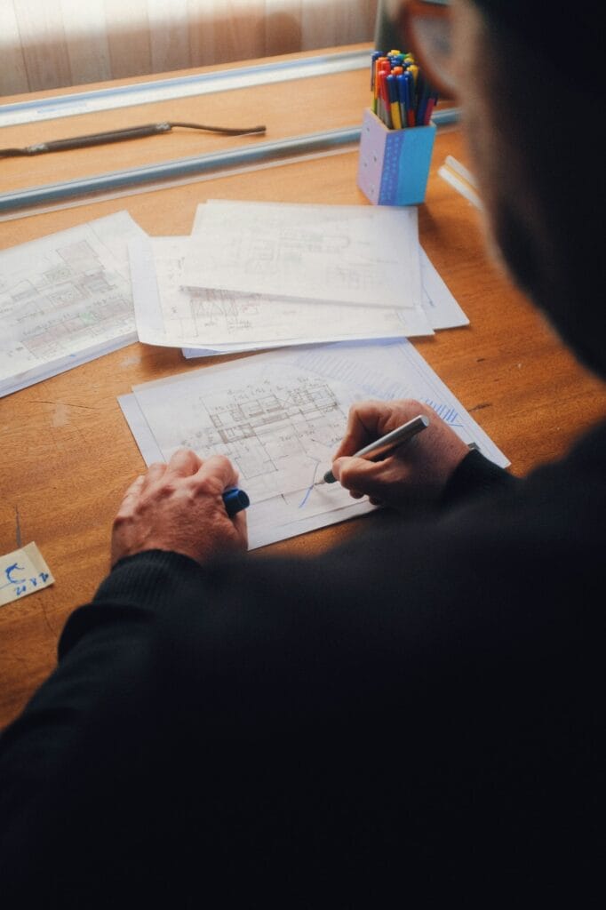 Illustrative library photograph, not an Elbaz project: an architect sketching a floor plan by hand over printed drawings