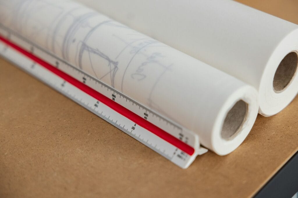 Illustrative library photograph, not an Elbaz project: rolled construction drawings and tracing paper on a desk