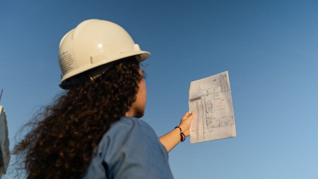 Illustrative library photograph, not an Elbaz project: a person in a hard hat holding up a drawing on site