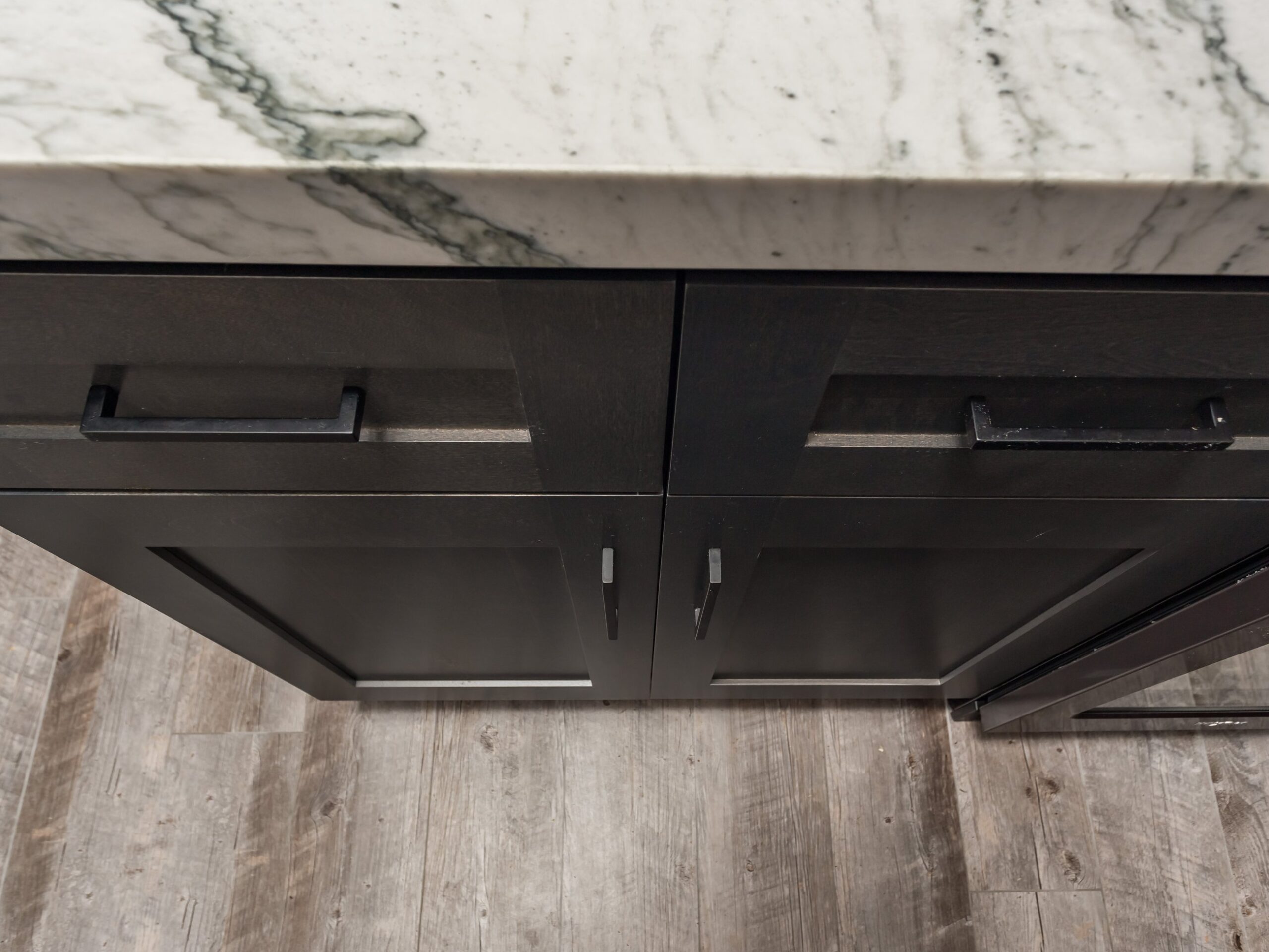 Close view of stained shaker door and drawer fronts with long bar pulls and a consistent reveal