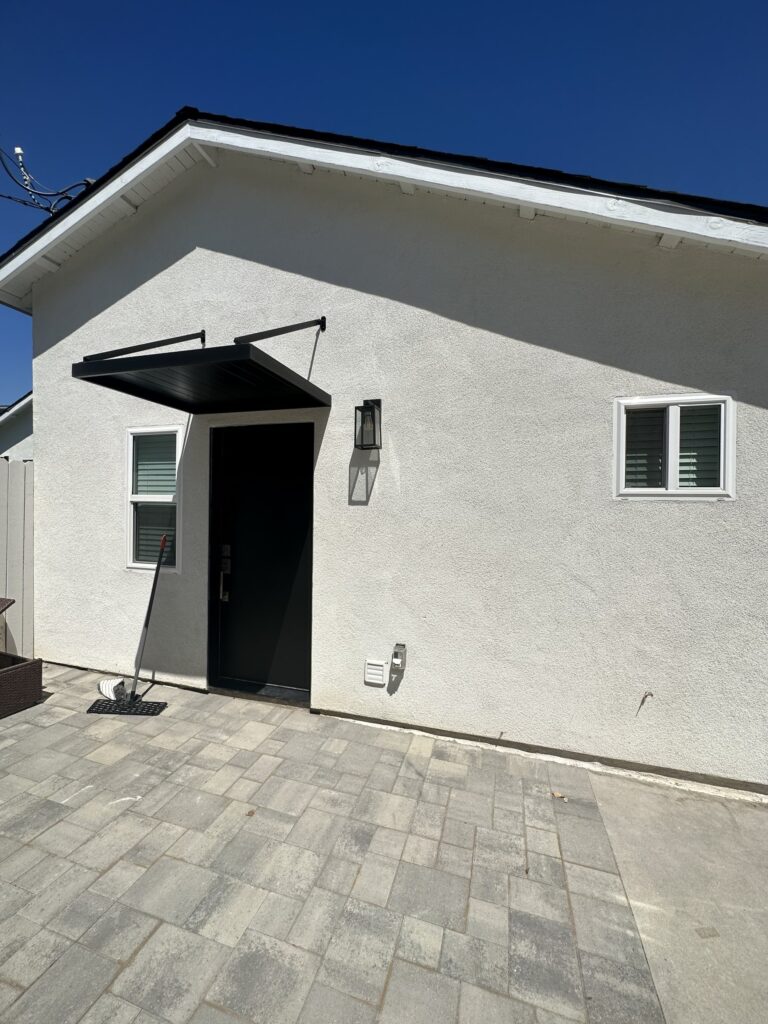 Private entrance to the studio ADU under a black awning, opening onto a paver terrace