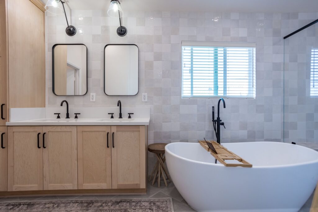 Double vanity in light oak beside a freestanding tub under a clerestory window