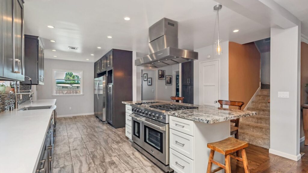 Grey shaker kitchen with a granite island and a stainless island hood, completed by Elbaz Construction in South Florida