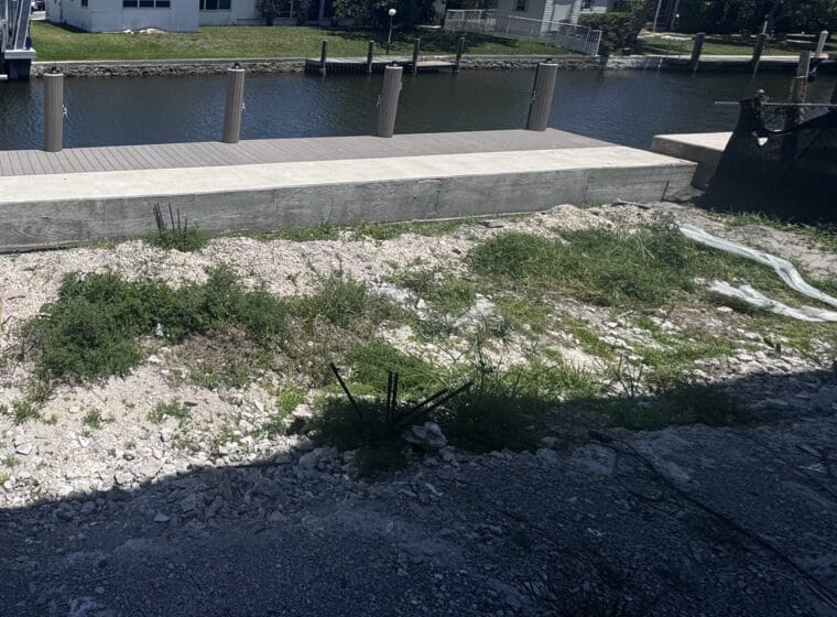 Canal frontage of the build site: new concrete seawall cap, composite dock and mooring piles, with the lot rough-graded behind it