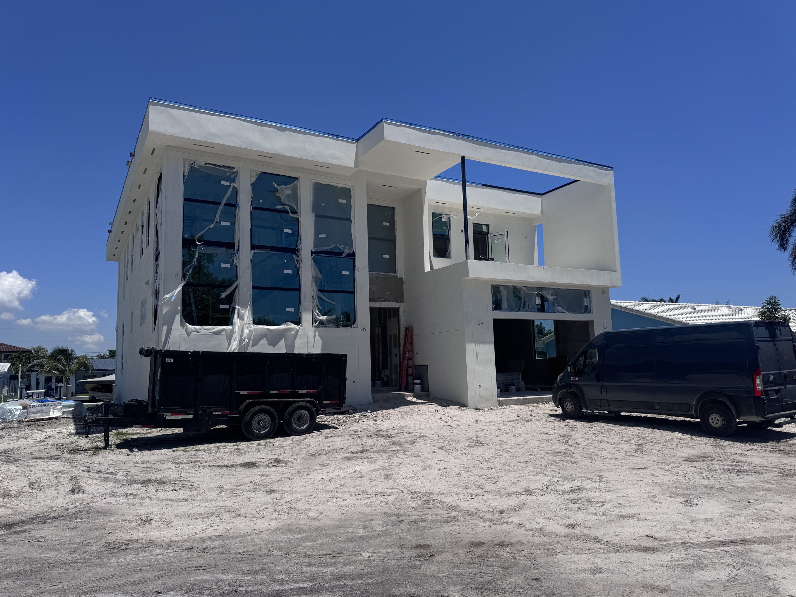 Two-storey Elbaz Construction custom home under construction on a South Florida lot, with the window and door openings glazed and protective film still on the glass