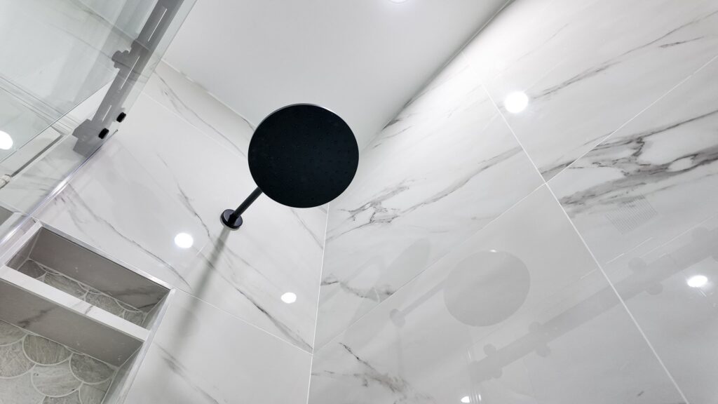 Rain head with the hand shower alongside it on the wet wall