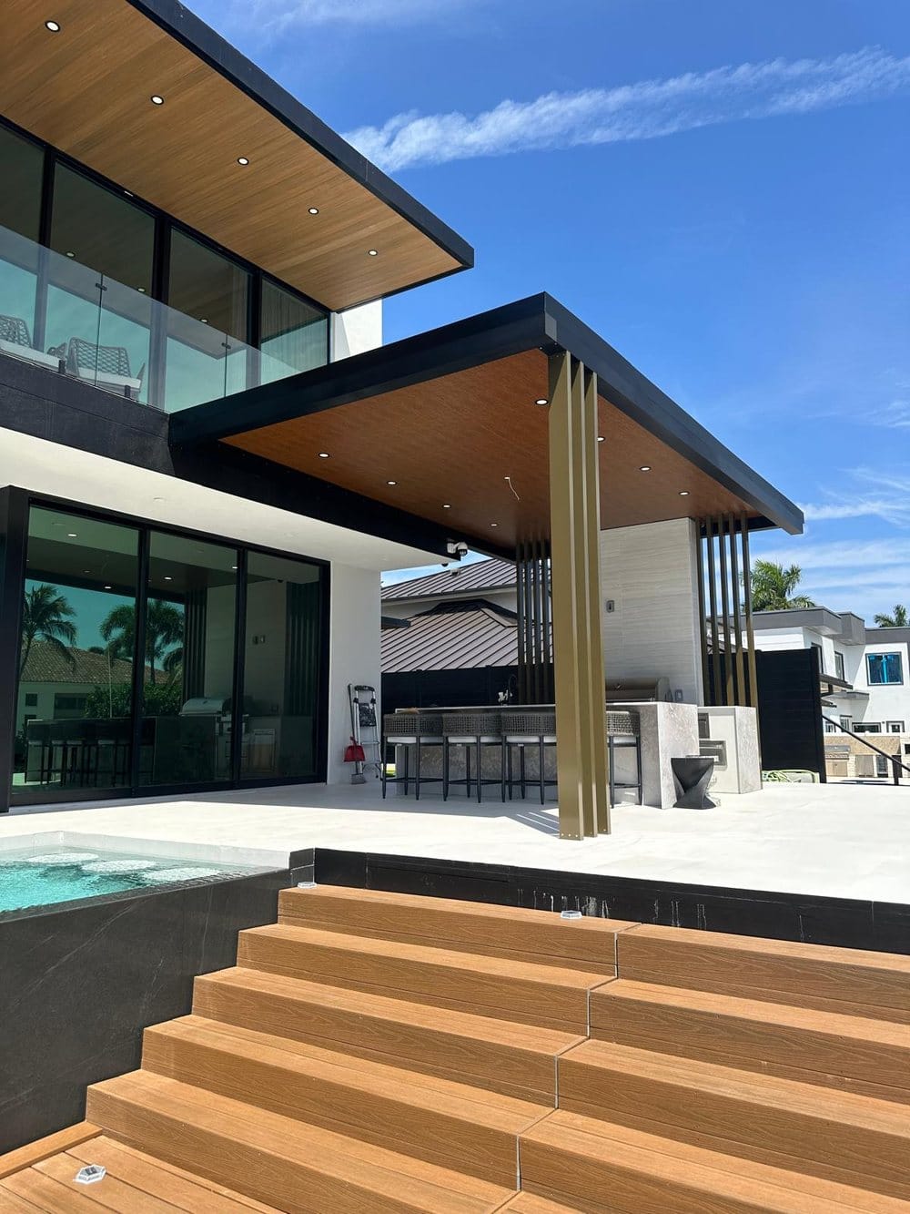 Timber steps rising from a spa to the covered terrace, with the paved deck and glazed elevation behind