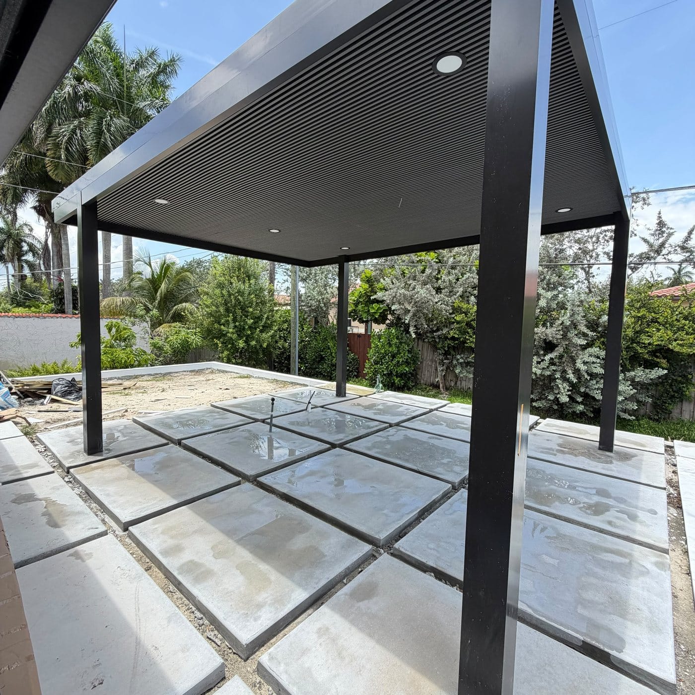Dark-framed canopy beside a pool with large-format pavers being set