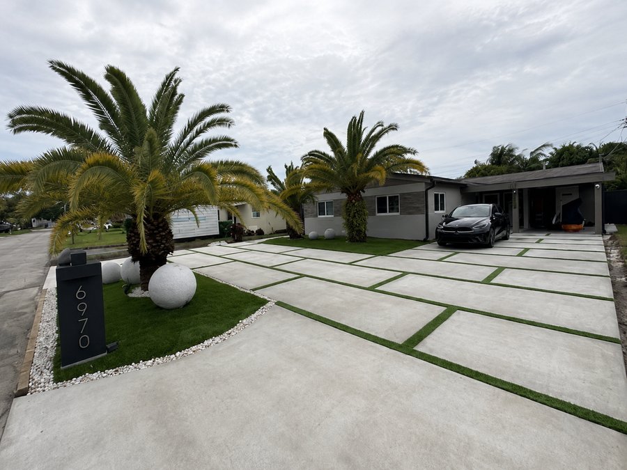 Poured concrete driveway panels separated by planted turf joints, with palms behind