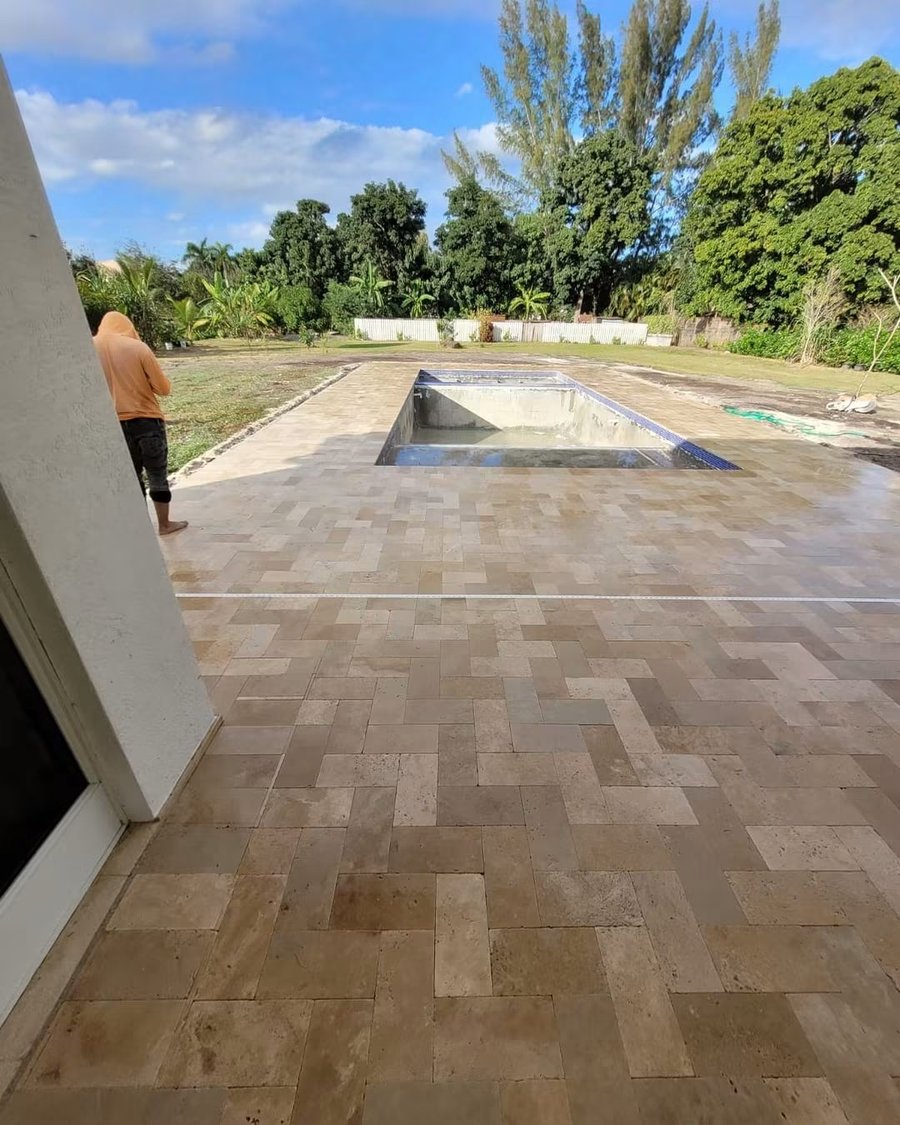 Large-format paving units being laid out on a prepared bed beside a pool