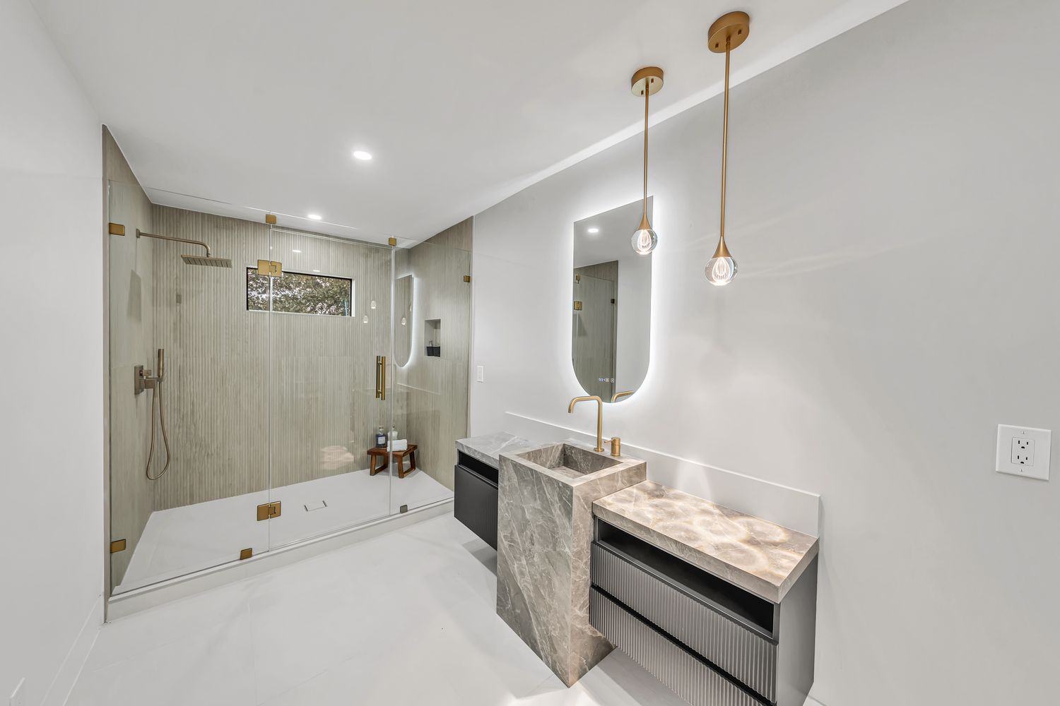 Walk-in shower with brass fittings alongside a stone-topped vanity in a completed bathroom