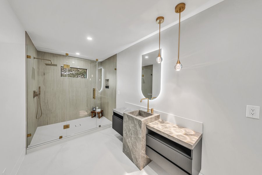 Walk-in shower with brass fittings alongside a stone-topped vanity in a completed bathroom