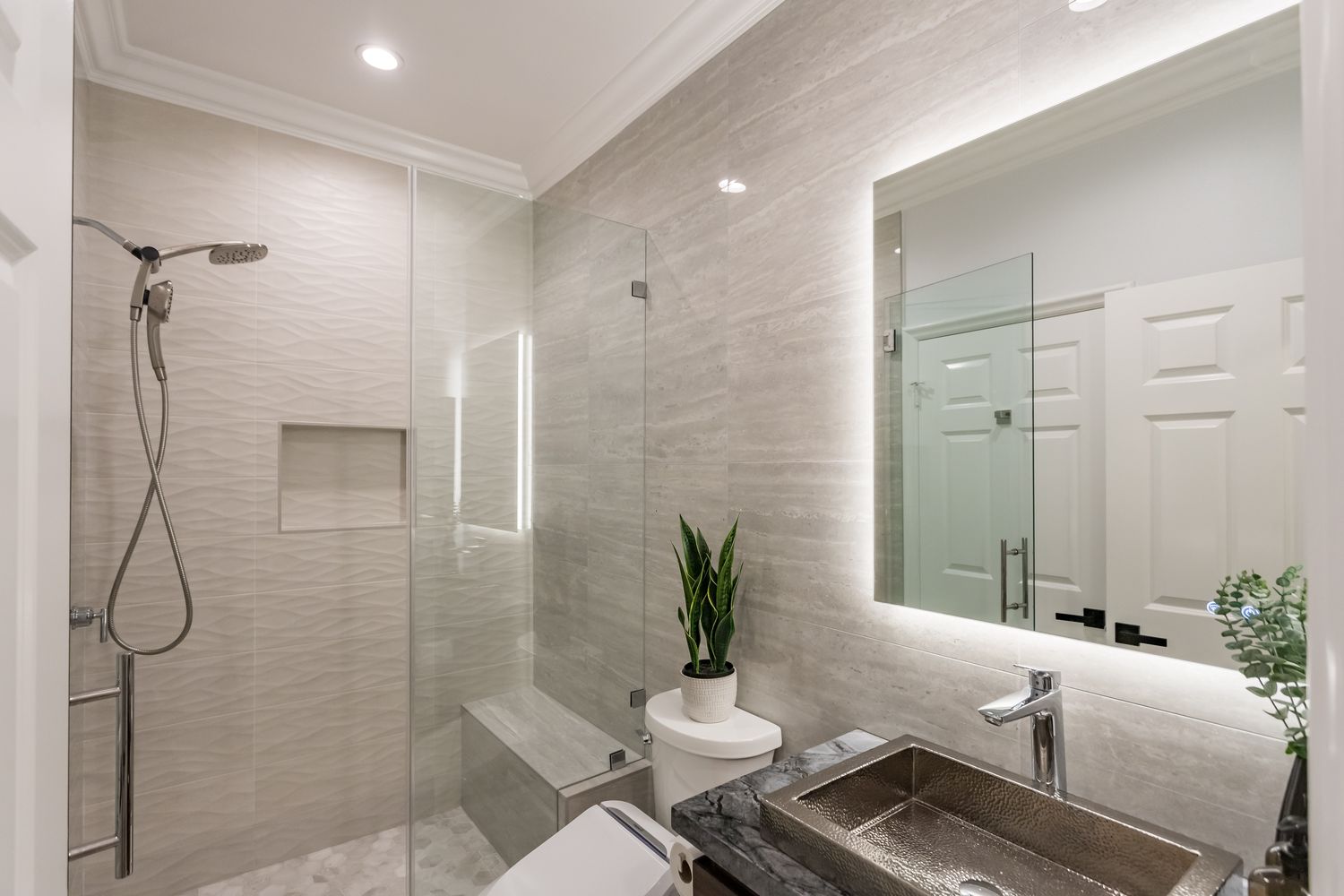 Completed bathroom with a hammered vessel basin, backlit mirror and a glazed walk-in shower