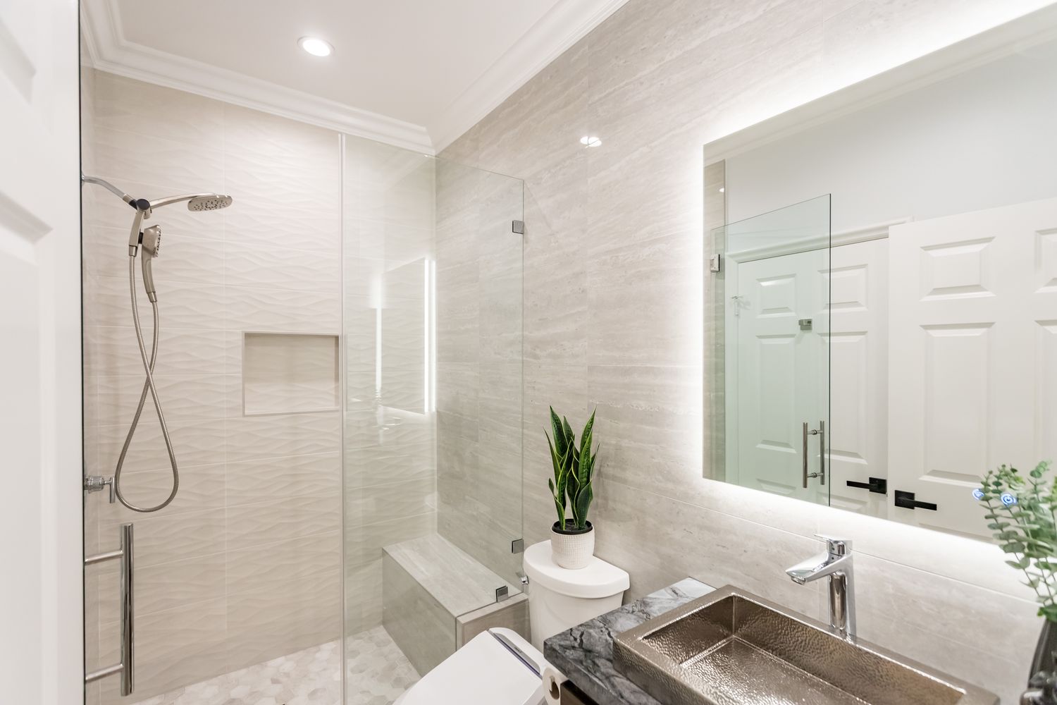 Walk-in shower behind a frameless glass panel with a recessed niche in large-format tile