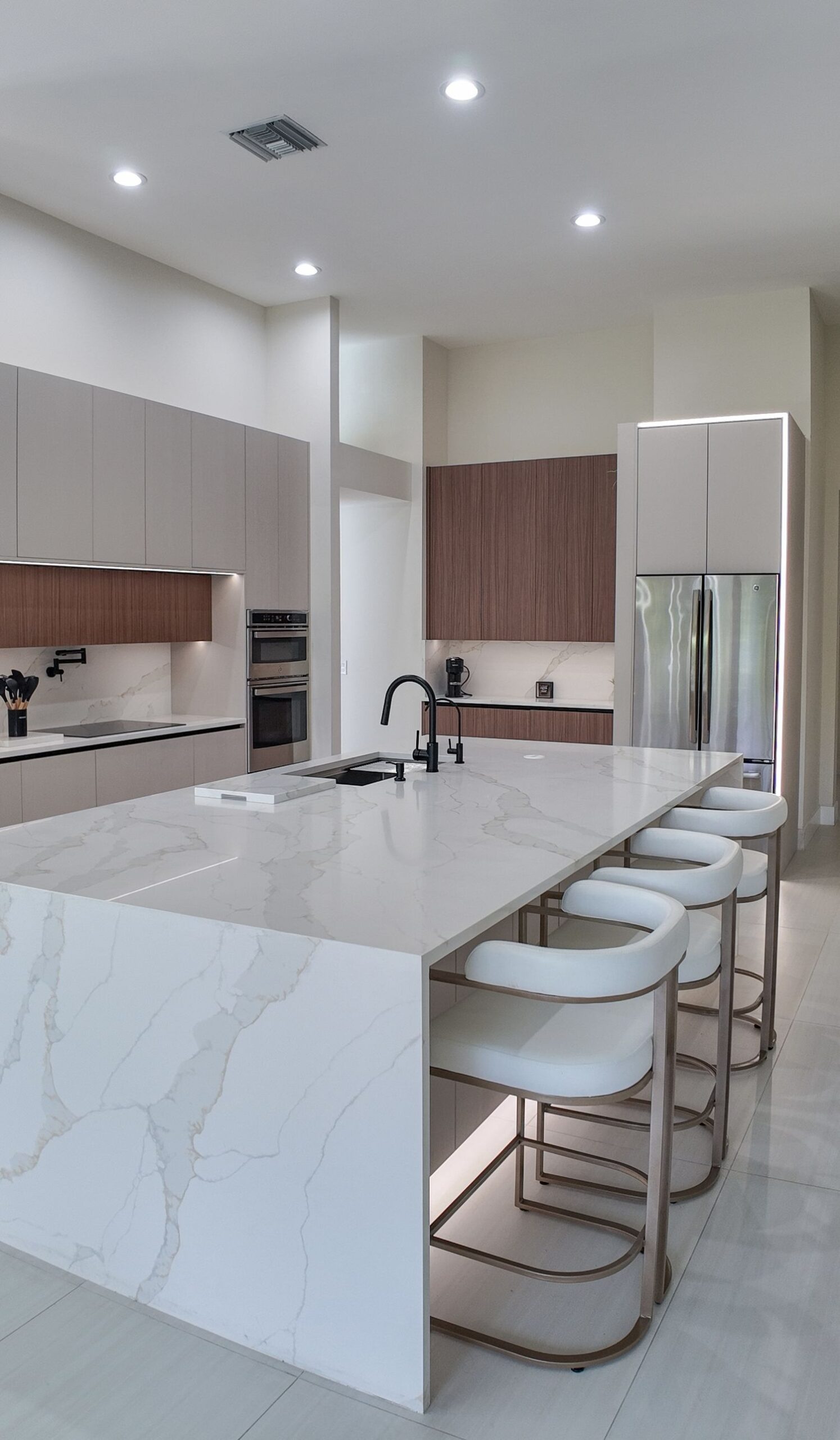 Seating side of a waterfall kitchen island, with three stools under a long stone overhang