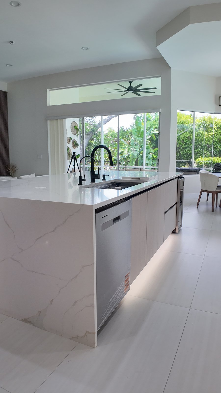 End of a waterfall kitchen island with an integrated dishwasher, looking out to the screened lanai