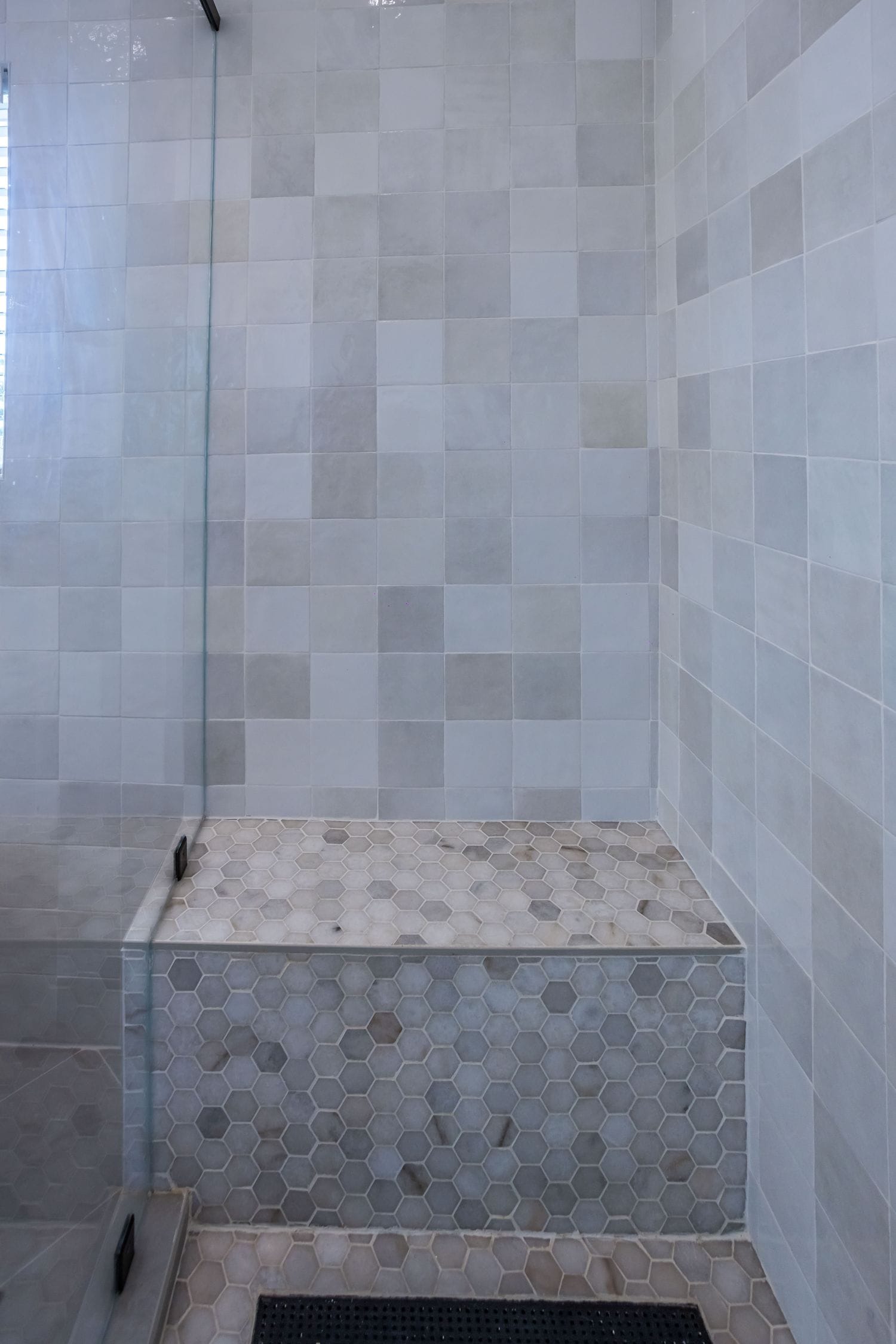 Corner shower bench in large-format tile above a hexagon mosaic floor