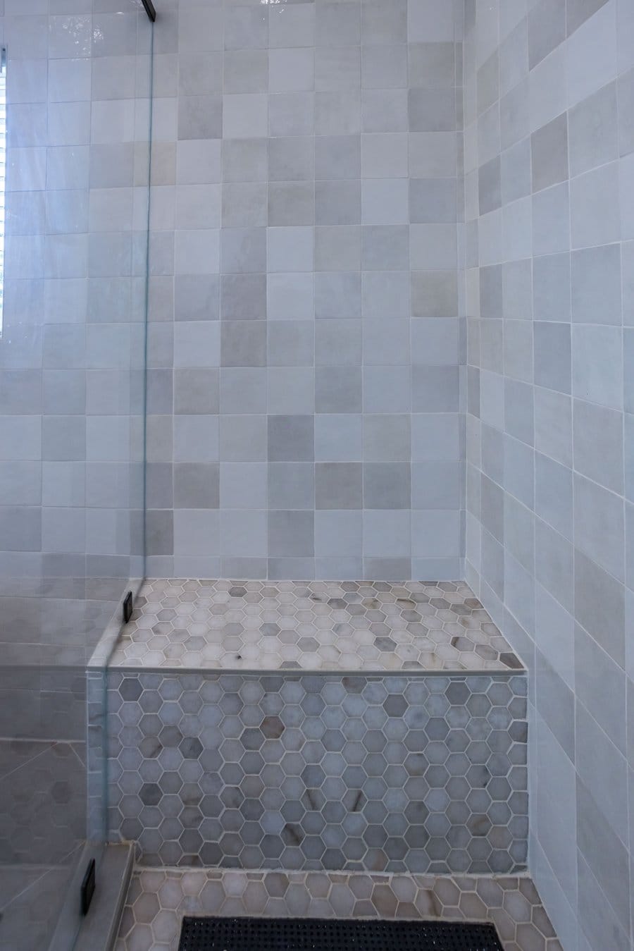 Corner shower bench in large-format tile above a hexagon mosaic floor