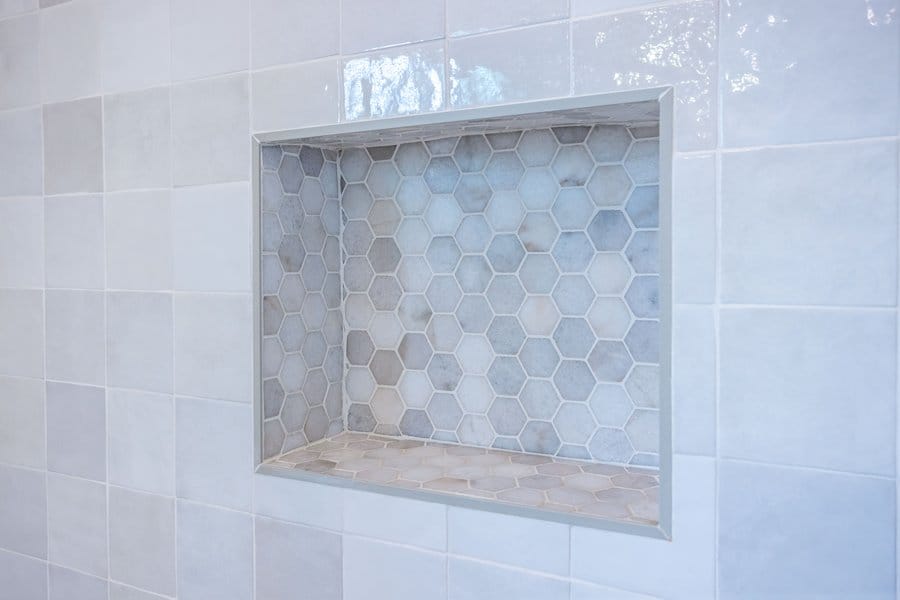 Recessed shower niche backed in hexagon mosaic within large-format wall tile