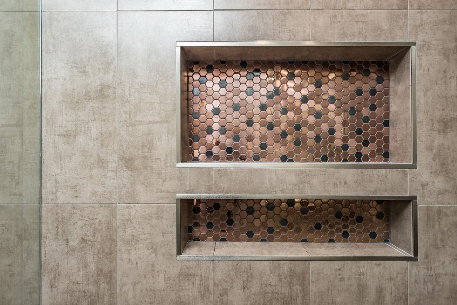 Two stacked recessed shower niches backed in copper-toned mosaic