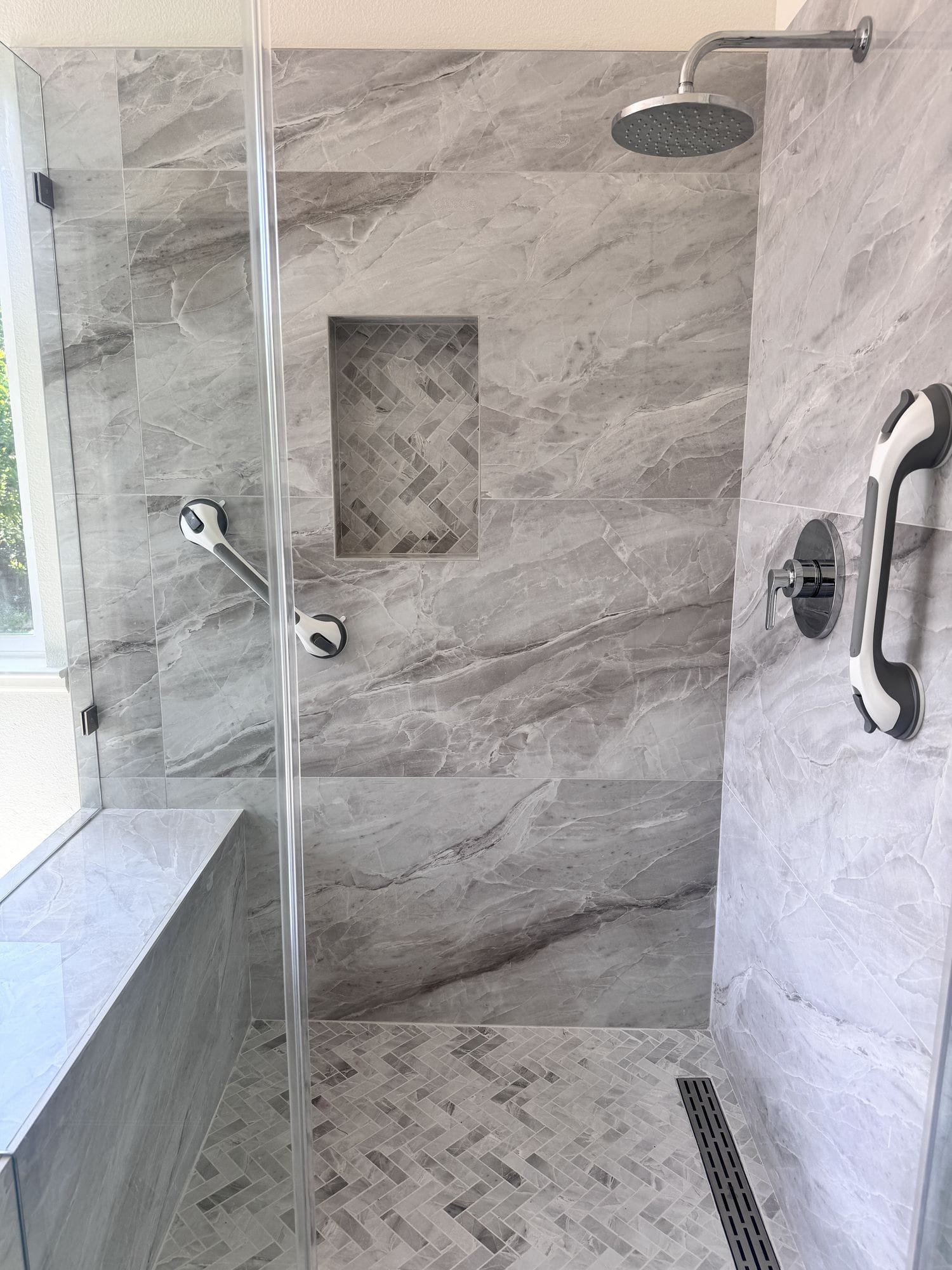 Rain shower head above a recessed niche set into marble-look porcelain wall tile