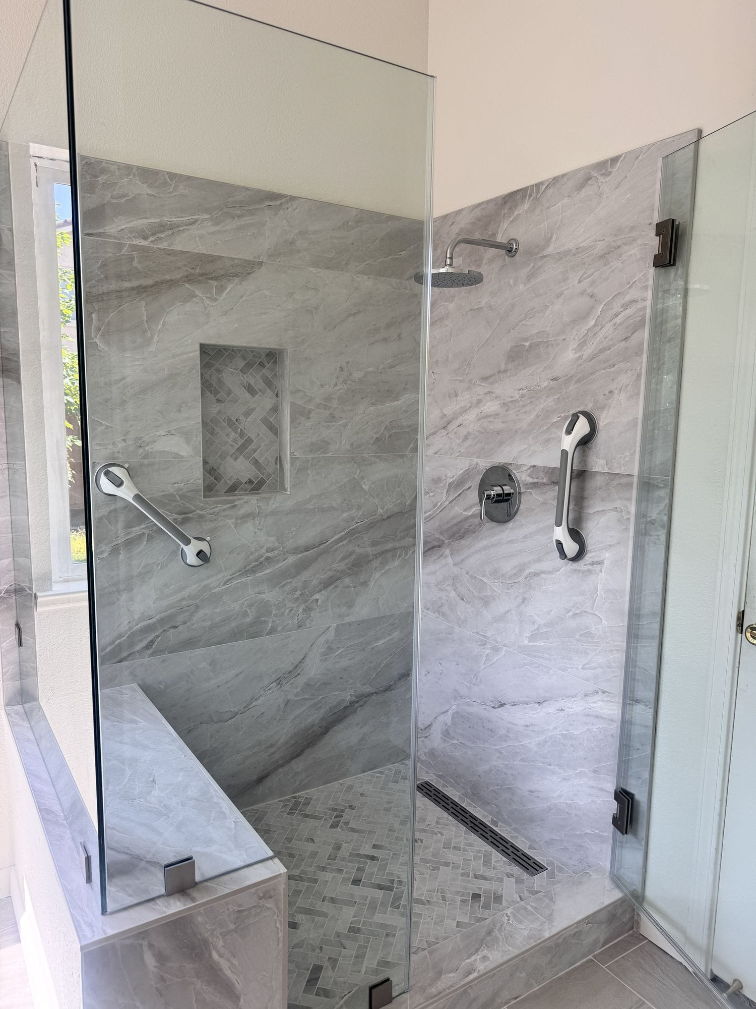 Two stainless grab bars fitted either side of a walk-in shower with a handheld shower on a slide bar