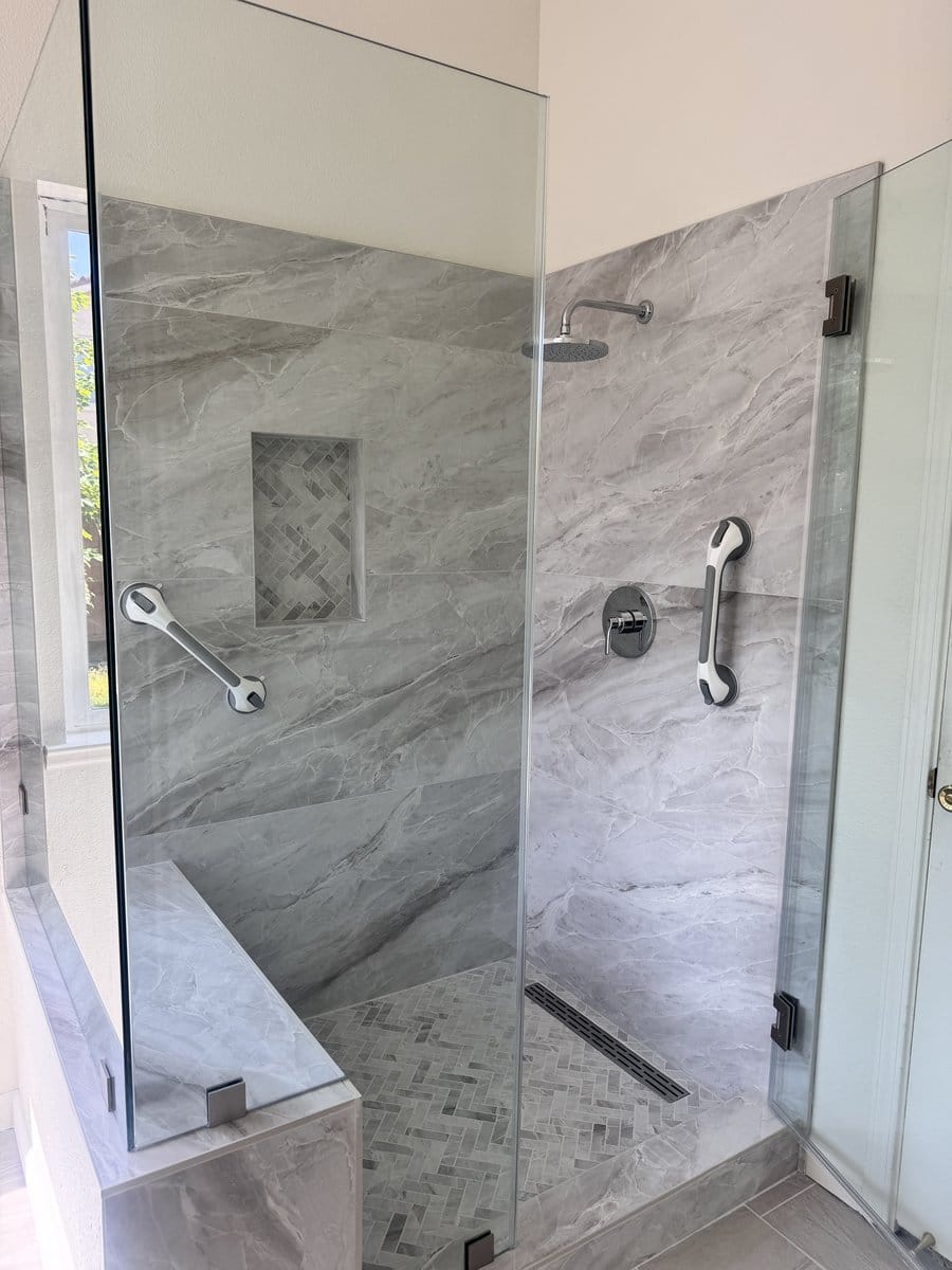 Two stainless grab bars fitted either side of a walk-in shower with a handheld shower on a slide bar