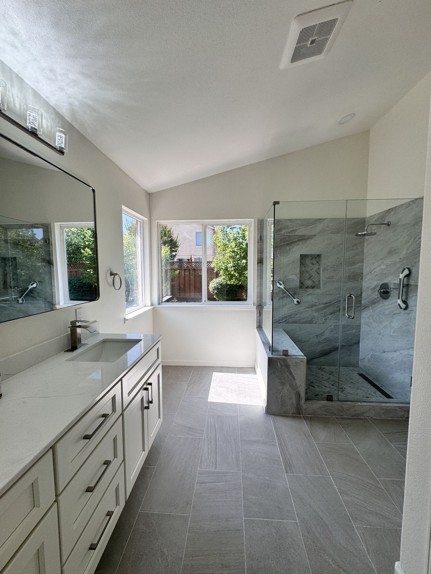 Primary bathroom with a vaulted ceiling, long vanity and glass-enclosed walk-in shower