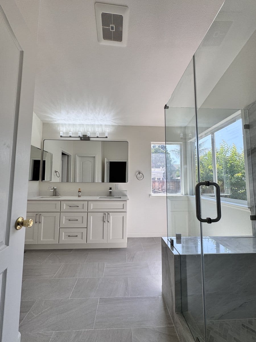 Frameless glass shower door with a brushed handle beside a tiled bench return