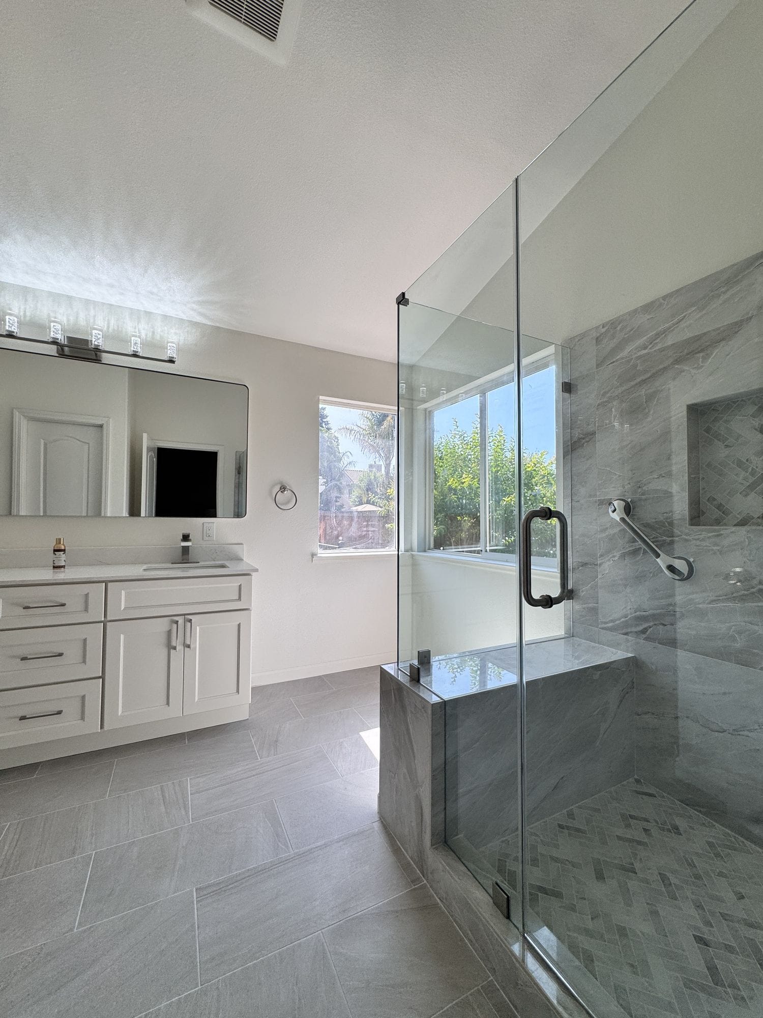 Walk-in shower enclosure viewed across the bathroom floor, glass panel and bench visible