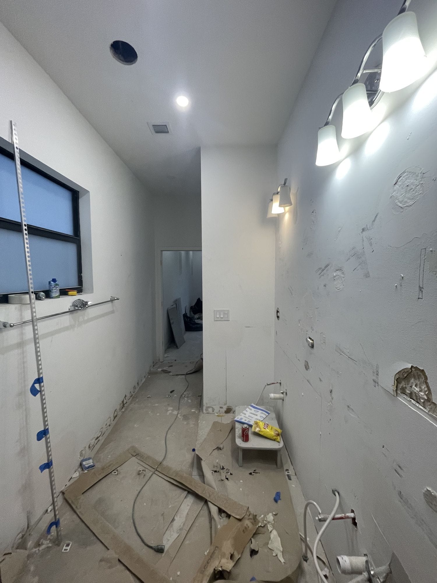 Bathroom mid-construction with plumbing rough-in exposed, a laser level on the wall and the floor screeded
