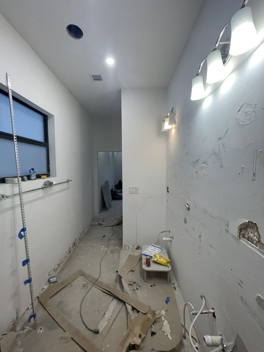 Bathroom mid-construction with plumbing rough-in exposed, a laser level on the wall and the floor screeded