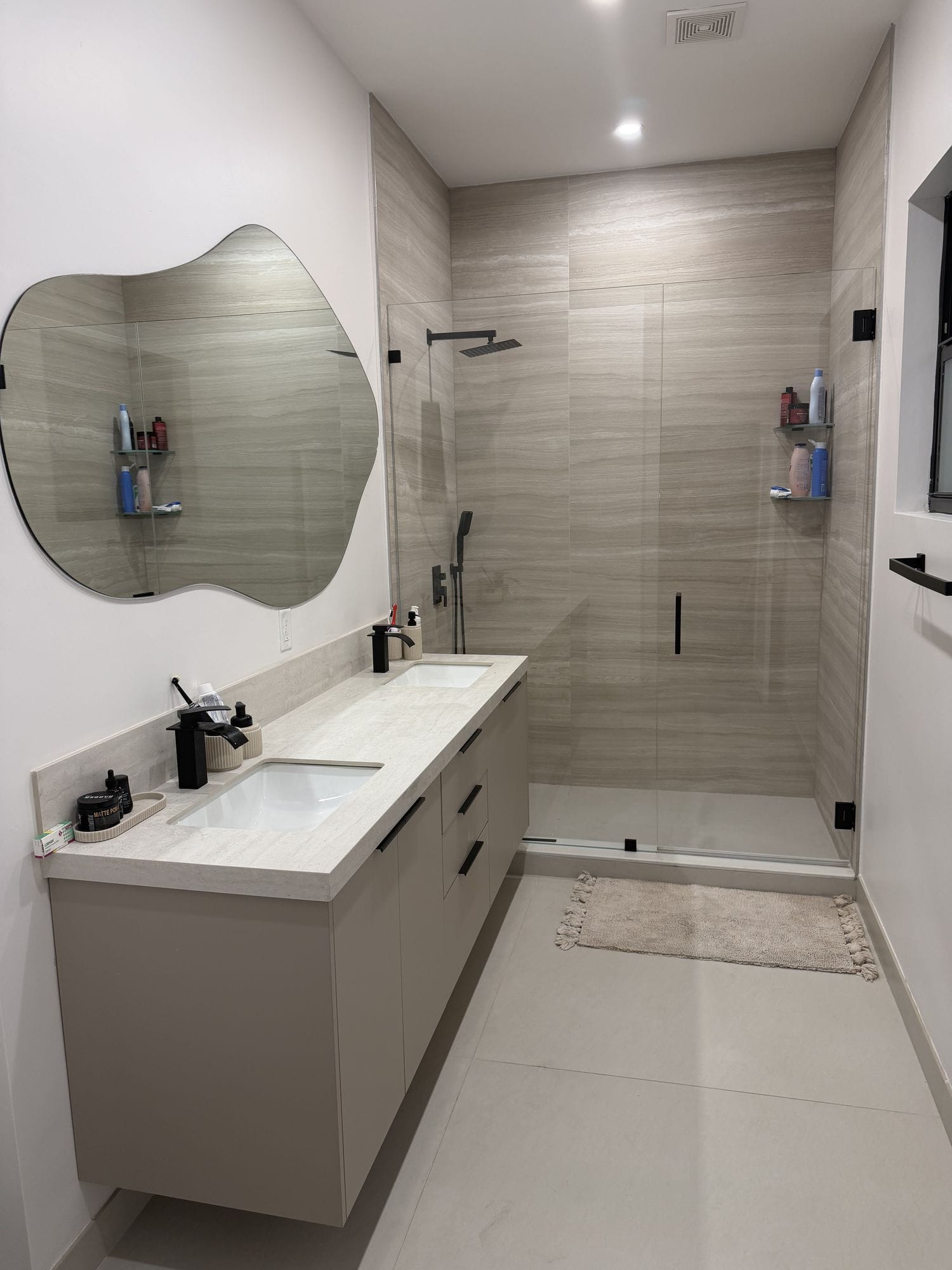 Curbless walk-in shower in stacked plank tile behind a frameless glass panel with black fittings