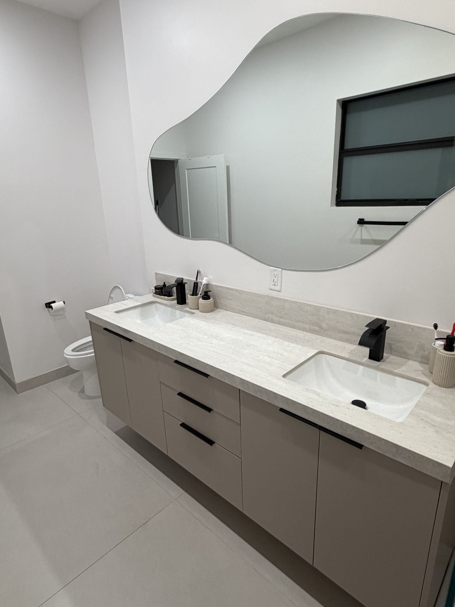 Floating vanity with twin basins, black taps and an organic-edge frameless mirror