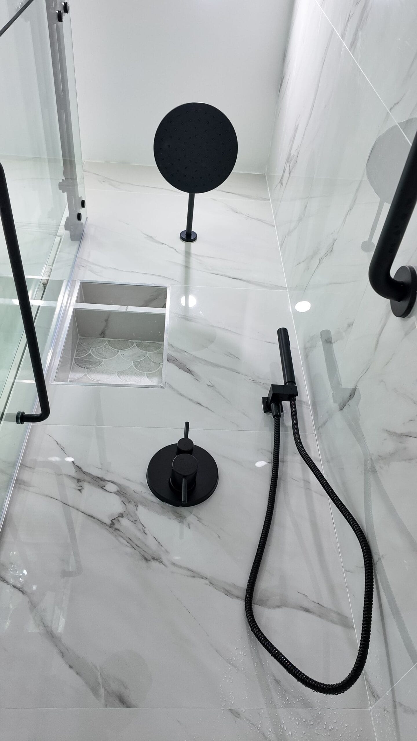 Black shower controls, handheld and grab bar against marble-look porcelain