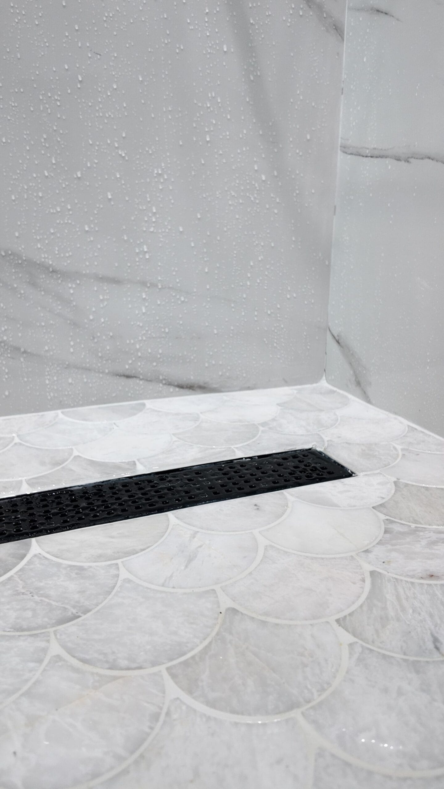 Black linear drain set into a scallop-pattern marble mosaic shower floor