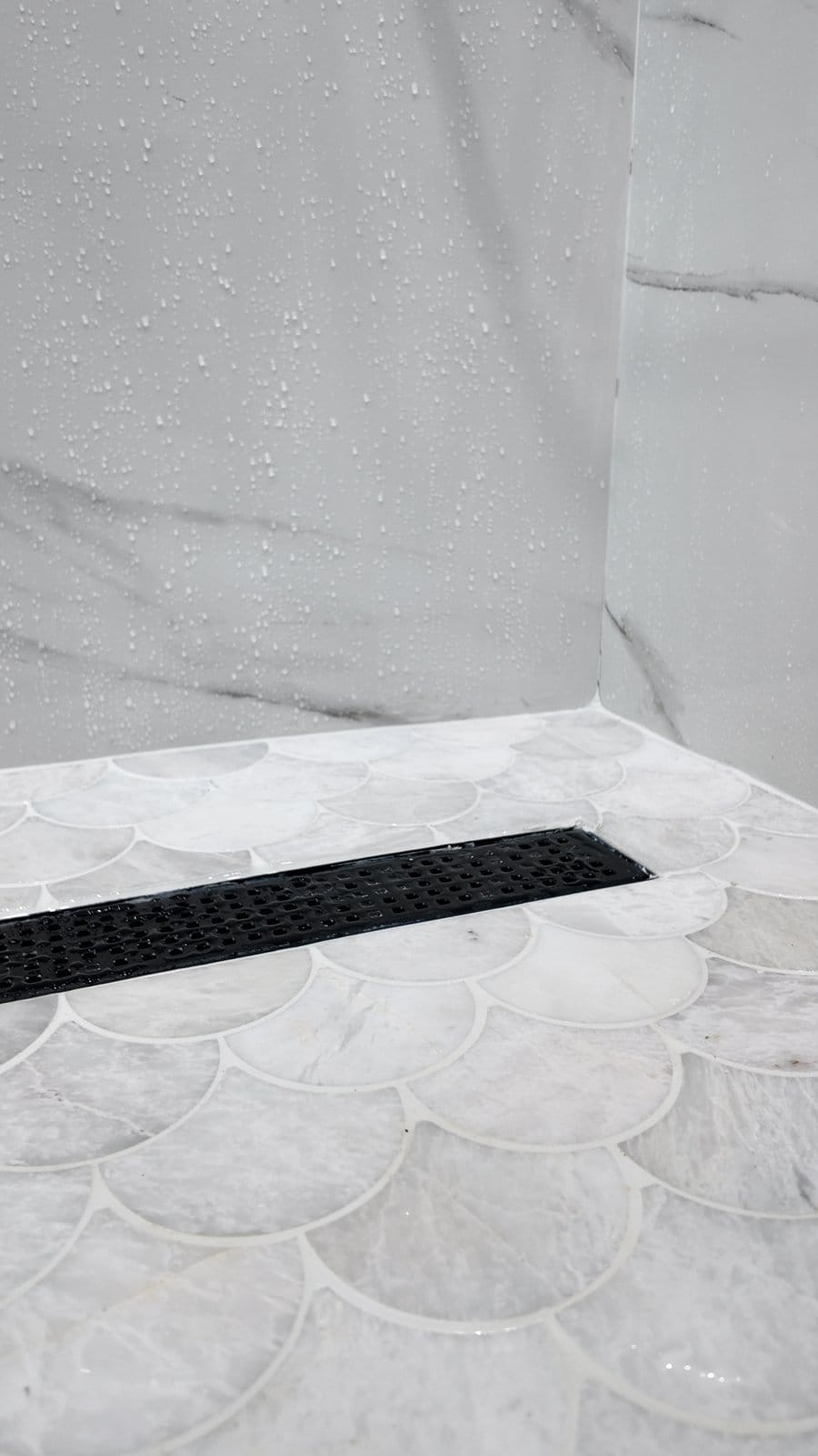 Black linear drain set into a scallop-pattern marble mosaic shower floor