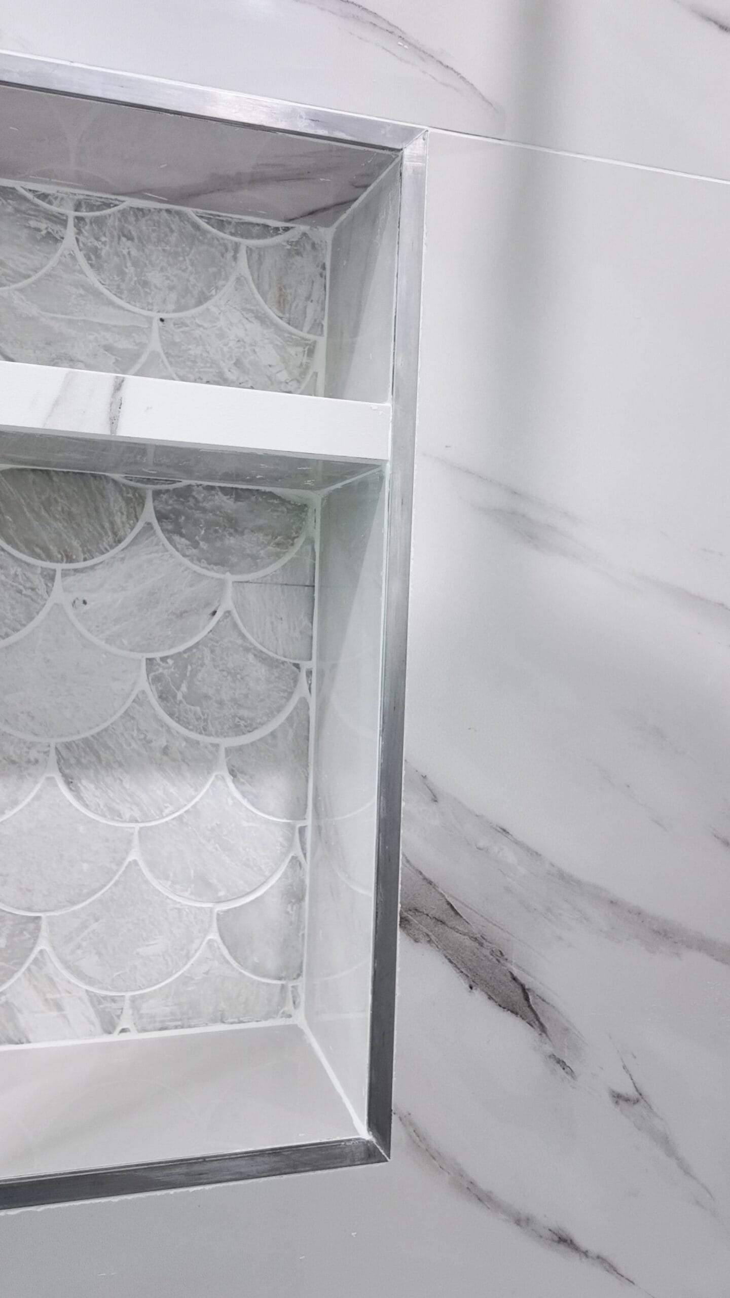 Recessed shower niche backed in scallop marble mosaic with a metal trim edge