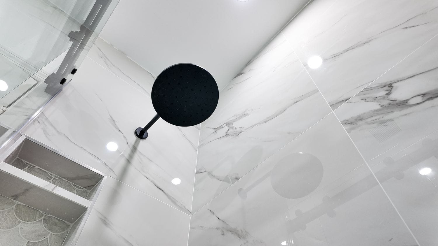 Black rain shower head mounted against a marble-look porcelain ceiling and wall