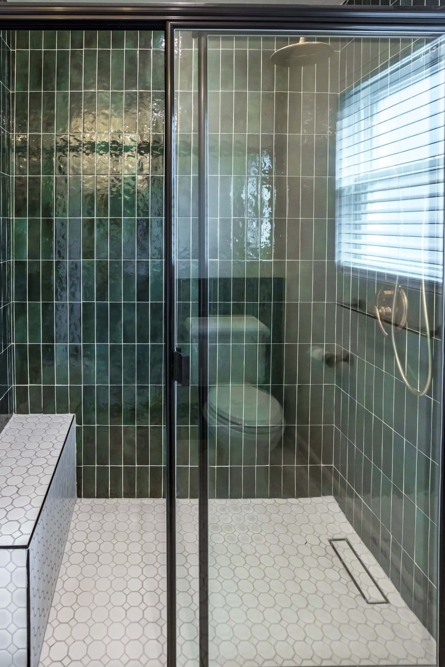 Walk-in shower in emerald green stacked tile with sliding glass, a white hexagon bench and a linear drain