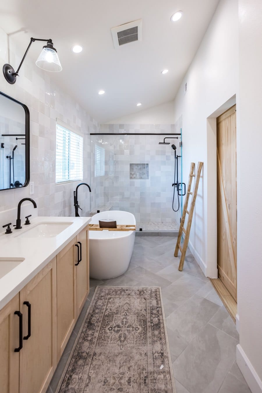 Long primary bathroom with a light oak vanity, freestanding tub and a glazed walk-in shower at the far end