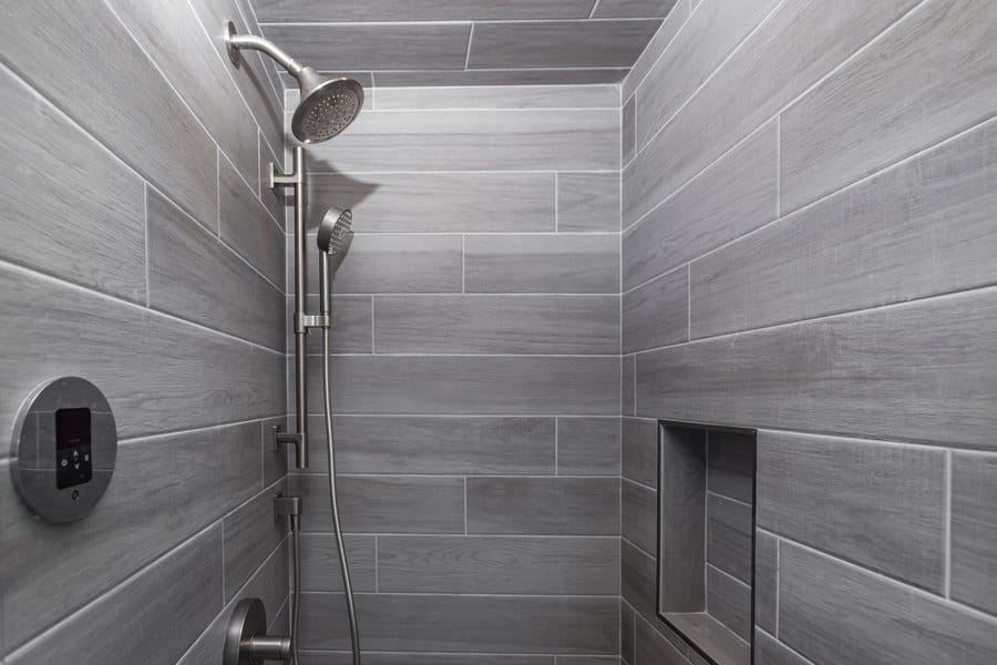 Walk-in shower lined in grey wood-look plank tile with a hexagon mosaic floor and brushed fittings