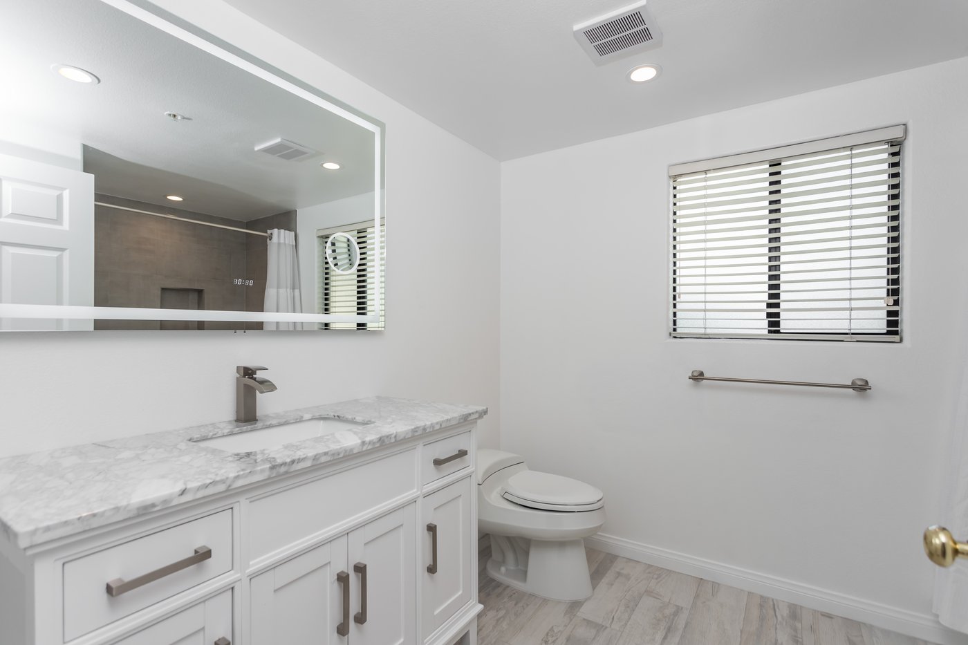 Bathroom with a wall-mounted grab bar beside the toilet, a white vanity with a stone top and wide clear floor space