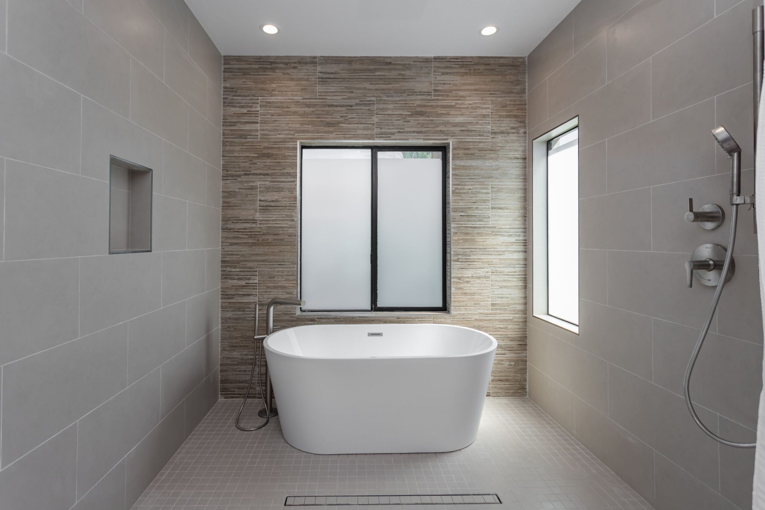 Shower area running level with the bathroom floor beside a freestanding bath, with a linear drain