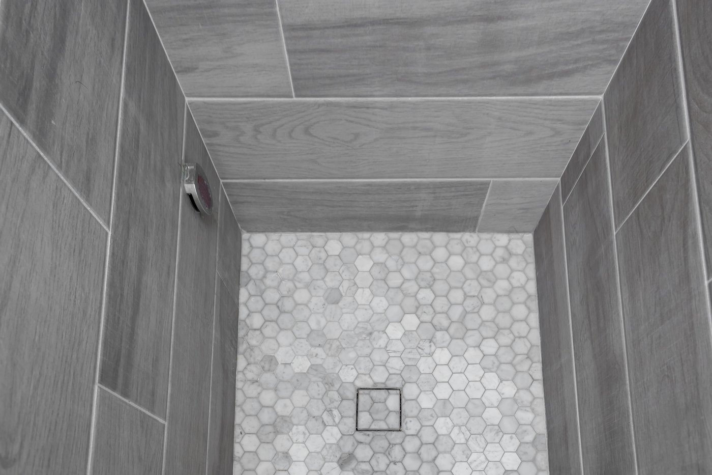 Shower floor in hexagonal mosaic meeting large-format wall tile, with a central drain